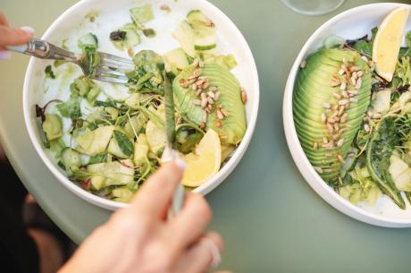 Overhead view of a woman eating a green salad with avocado, cucumber and toasted sunflower seeds 