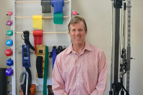 Mark Bussell, DPT, sits in front of physical therapy equipment